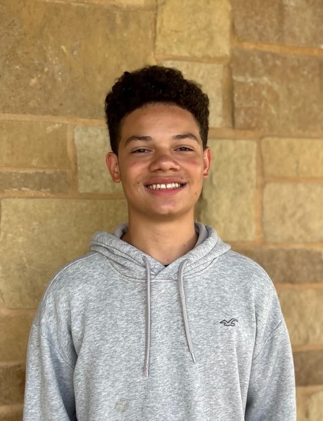 Dexter, a Valor Heights student, smiling in front of a stone wall
